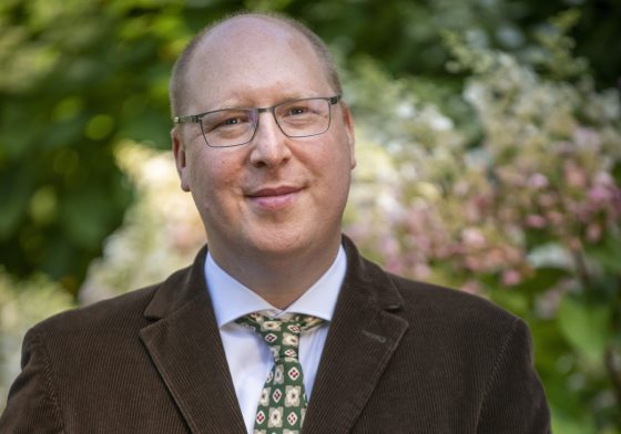 person in a brown suit with gray glasses looking at the camera